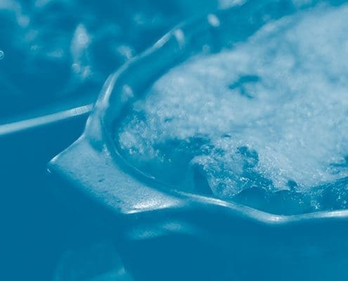 Blue-tinted close-up of a pot of boiling liquid with foam on top.